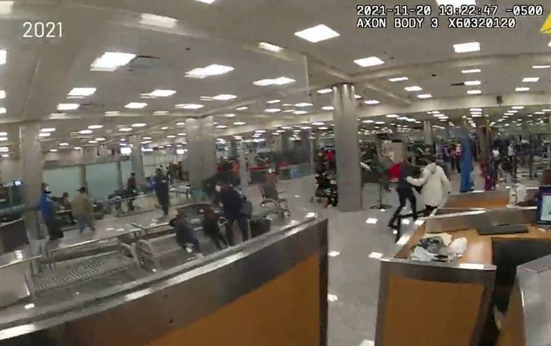 A still from body camera footage from a law enforcement officer shows a chaotic scene of a large crowd of people in the security checkpoint area running in different directions.