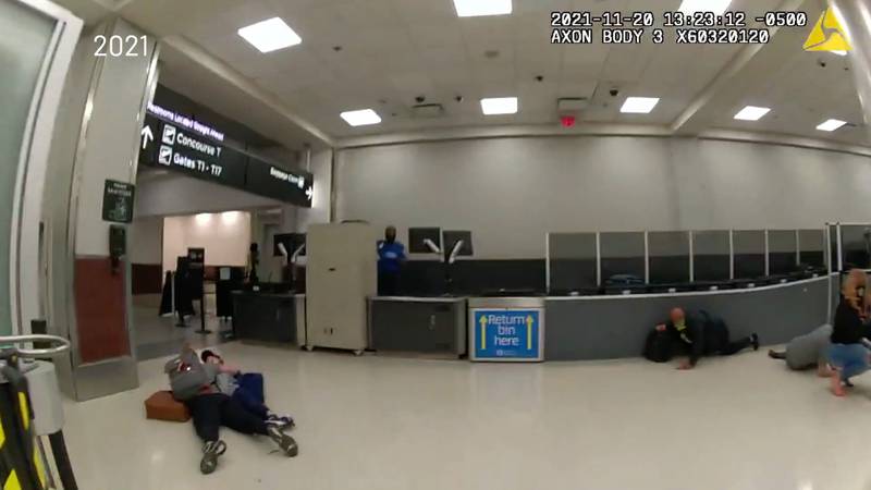 Passengers at the Atlanta airport lie on the ground or duck behind equipment in the security checkpoint in an image captured by a body camera worn by a law enforcement officer.